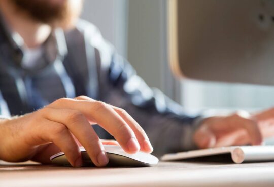 Closeup of man using mouse and laptop.
